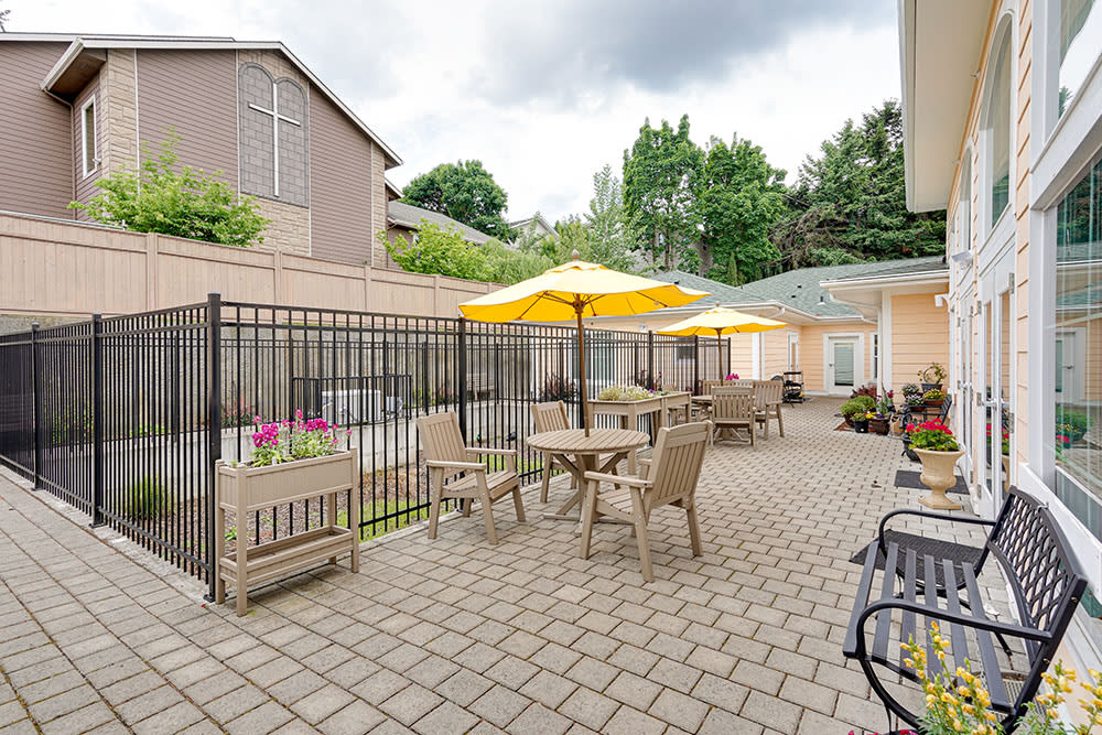 An outdoor patio area with tables, chairs, and yellow umbrellas set on a brick floor.