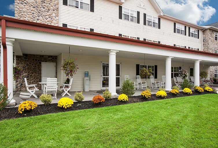 A building with a porch featuring columns, outdoor seating, and well-maintained landscaping.