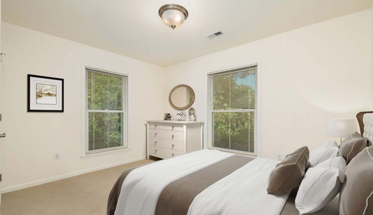 A neatly furnished bedroom with two windows and a dresser with a mirror.
