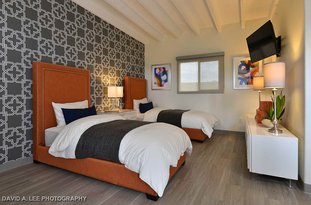 A modern bedroom with twin beds, featuring orange headboards and a stylish patterned wallpaper.