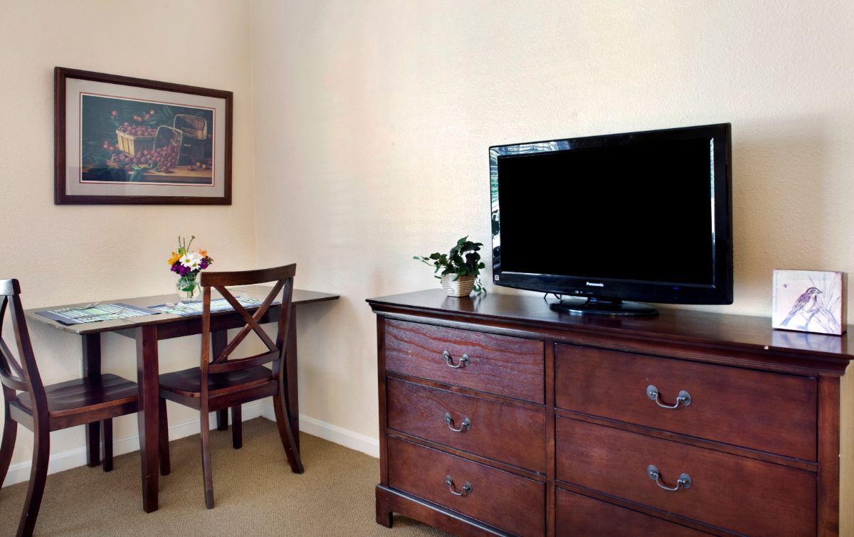 A cozy hotel room with a wooden dresser, television, desk, and chair.