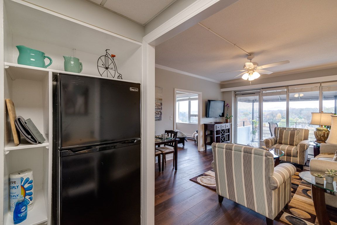 A cozy open floor plan featuring a kitchen with a black refrigerator, adjacent to a living room with hardwood floors and a ceiling fan.