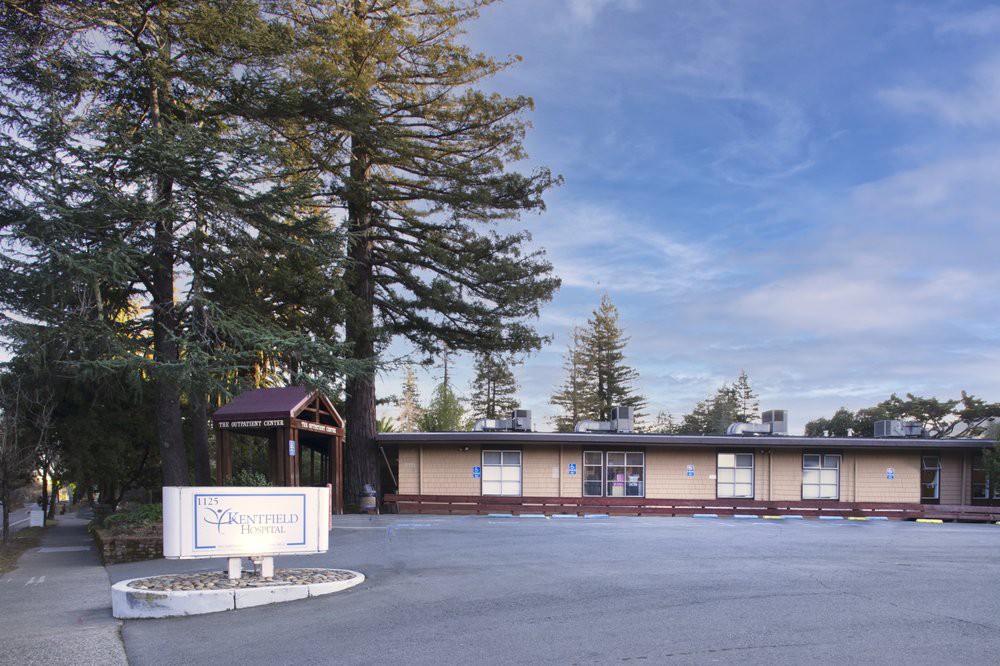 A small building surrounded by tall trees under a clear sky.