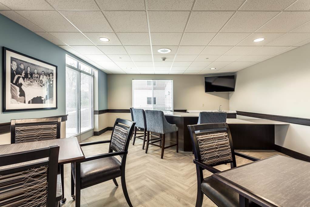 A modern conference room with tables, chairs, and a TV screen under ample natural light.