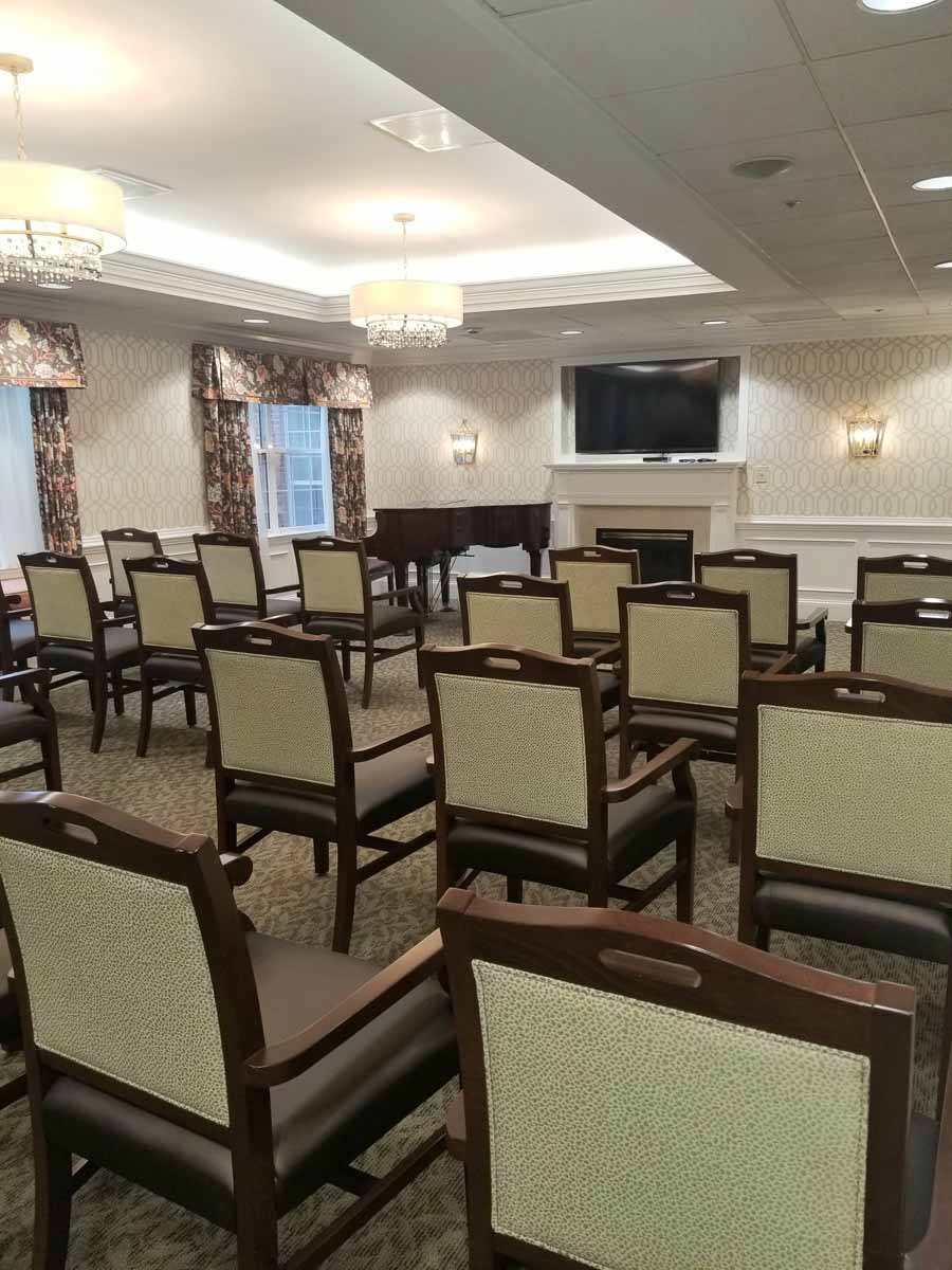 A small conference room with rows of chairs, a piano, and a mounted television.