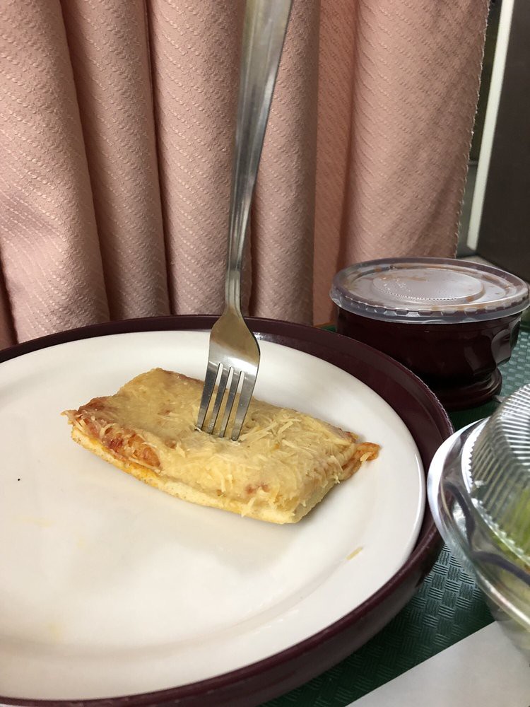 A pancake pierced by a fork, ready to be served with a side of syrup.