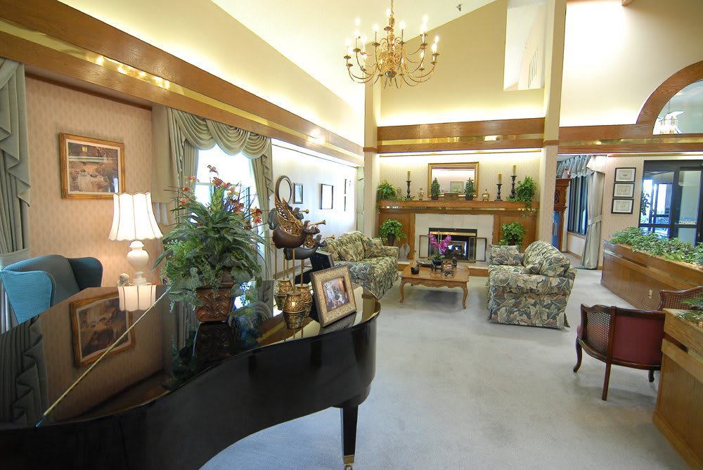 A spacious living room featuring a grand piano, elaborate chandelier, and cozy fireplace.