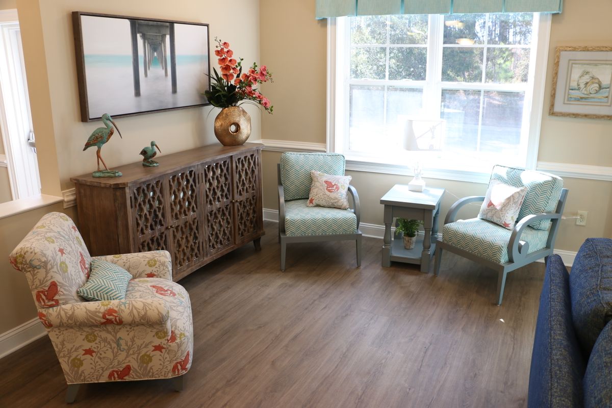 A cozy living room with comfortable armchairs, wooden flooring, and natural light streaming through the window.