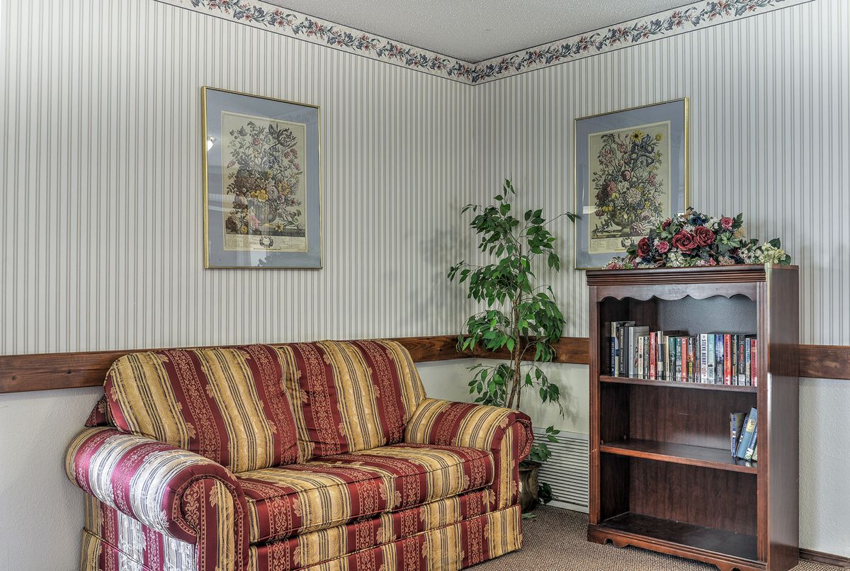 A cozy living room corner featuring a striped sofa, wallpapered walls with framed artwork, an indoor plant, and a bookshelf.