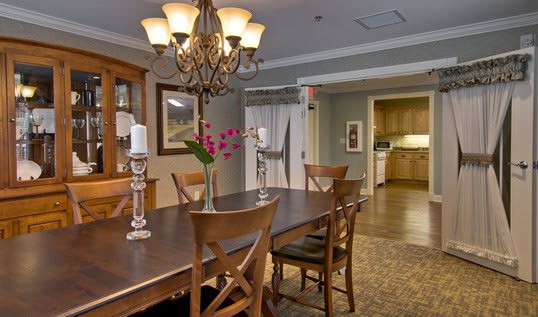 A warmly lit dining room featuring a wooden table and chairs, with a chandelier overhead.