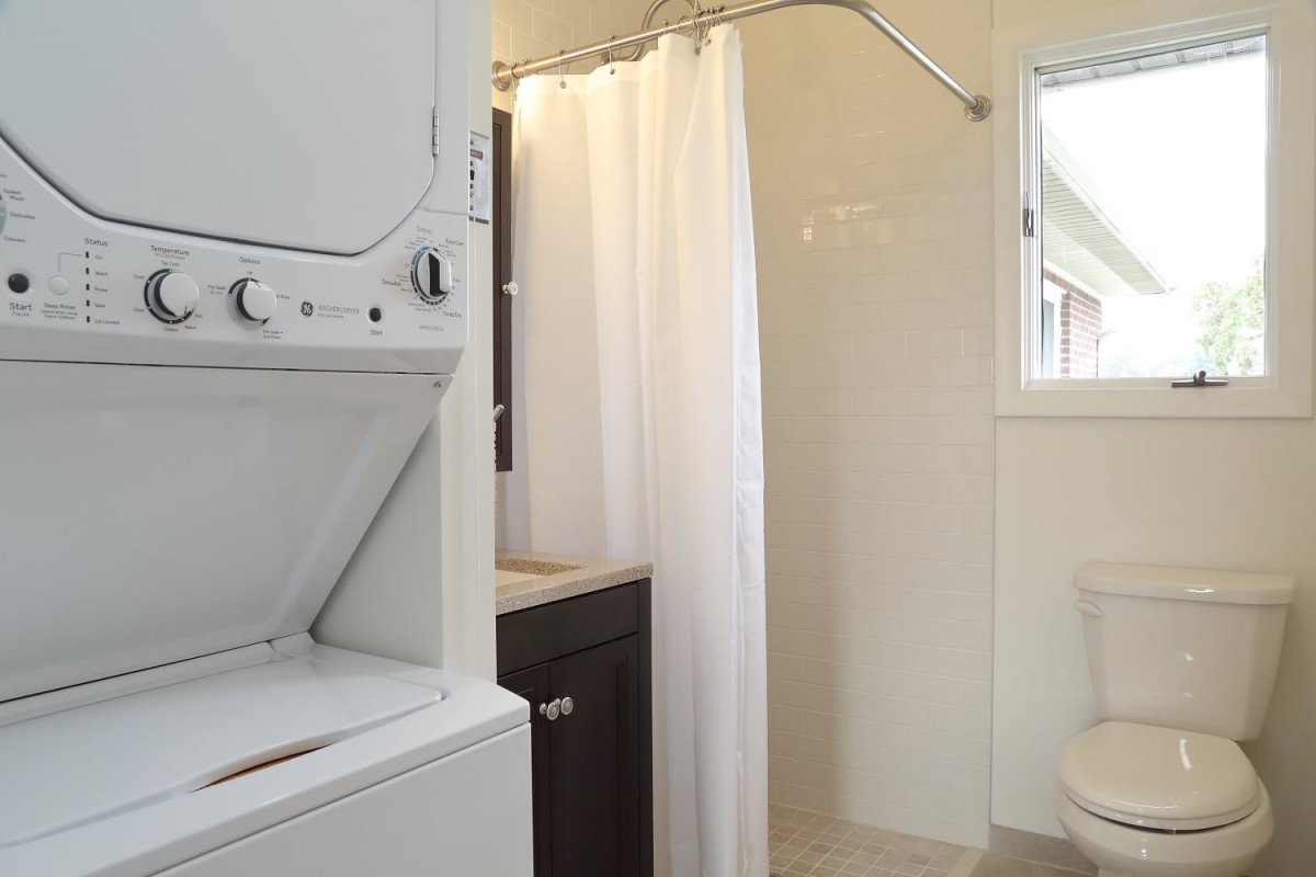 A small bathroom with a shower and stacked washer and dryer.