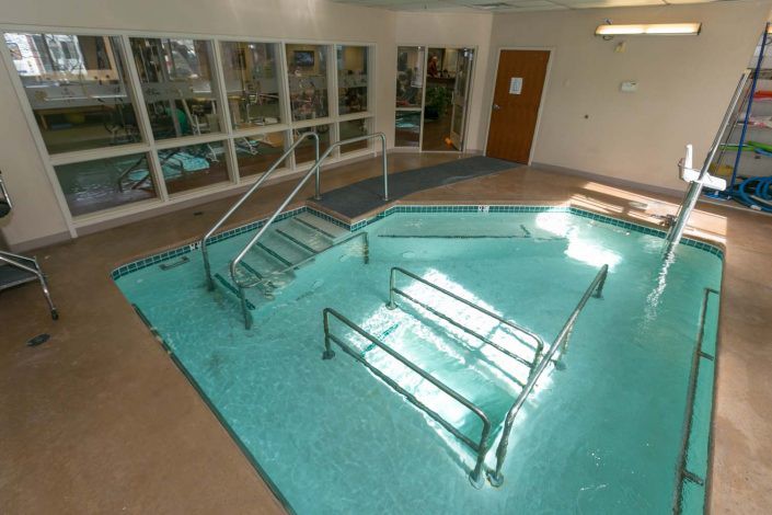 An indoor therapy pool equipped with handrails and steps for rehabilitation purposes.