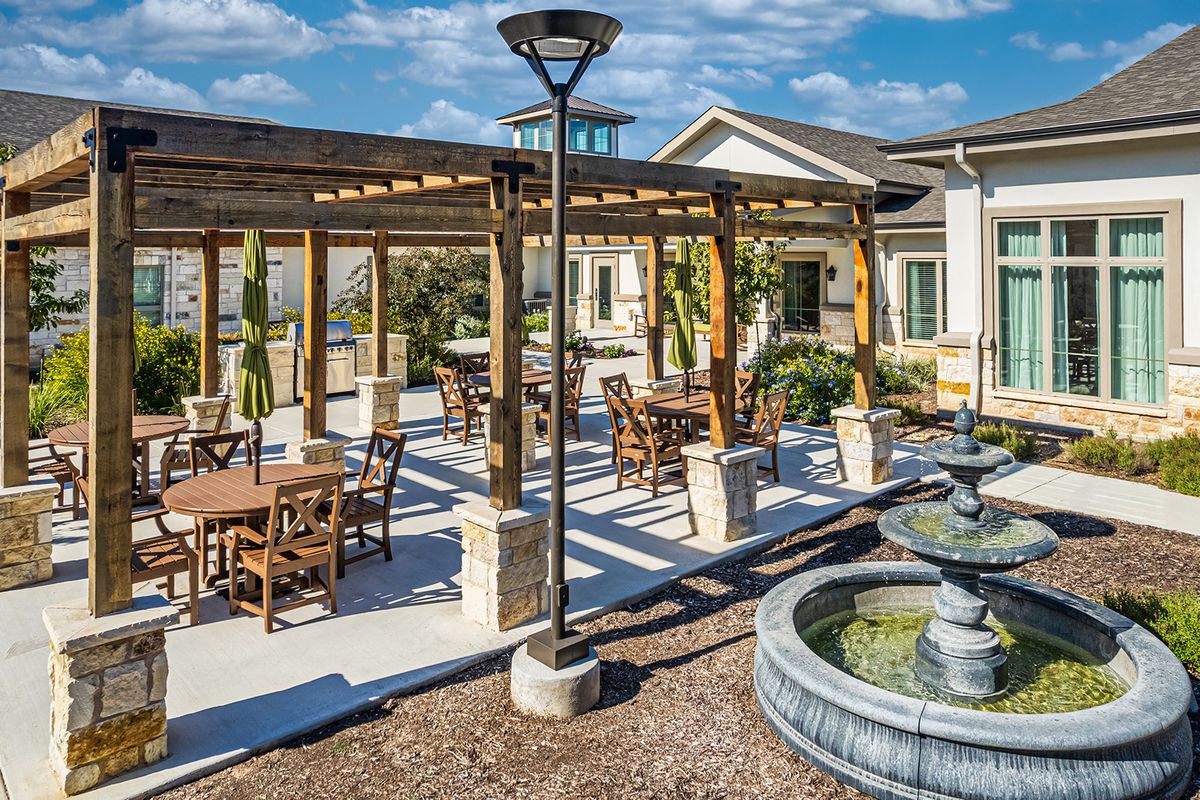 A sunny outdoor patio with a pergola, tables, chairs, and a decorative fountain.
