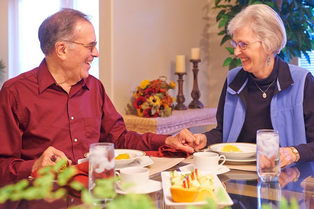 An elderly couple smiling and holding hands while dining together.