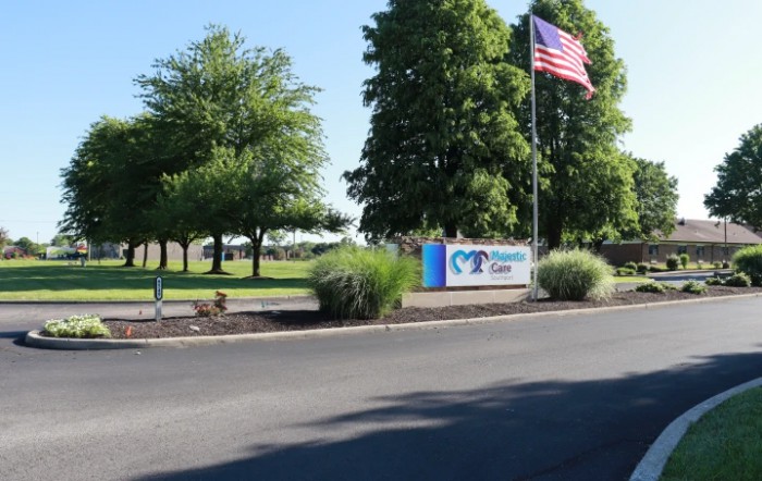 A scenic outdoor view featuring a company sign, an American flag, and lush green trees lining a road.
