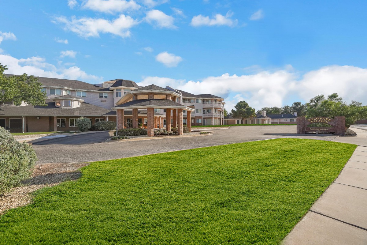 A large building with a driveway and well-maintained lawn under a clear blue sky.