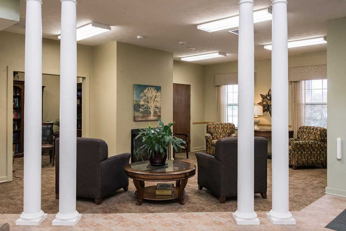 A cozy living room with comfortable seating around a central table, accented by artwork and decorative columns.