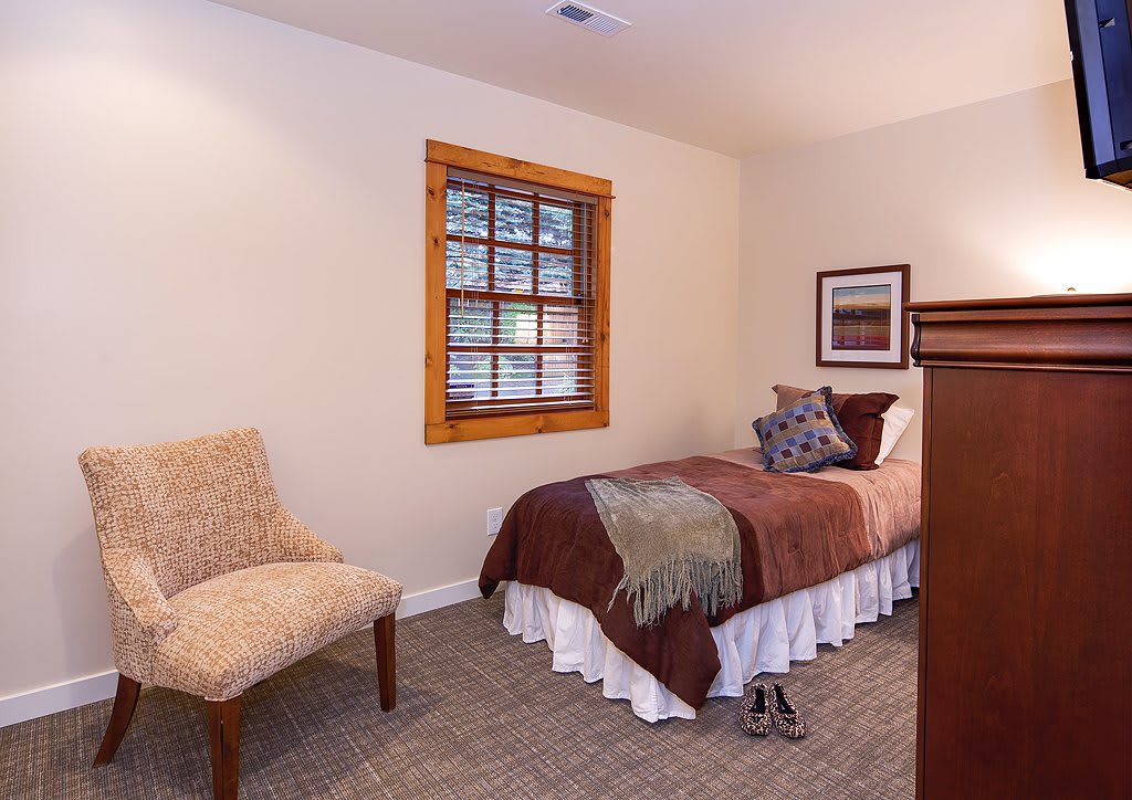 A cozy bedroom with a single bed, a chair, and a window featuring wooden blinds.