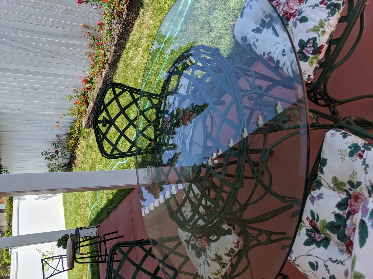 A glass patio table with metal chairs in a garden setting.