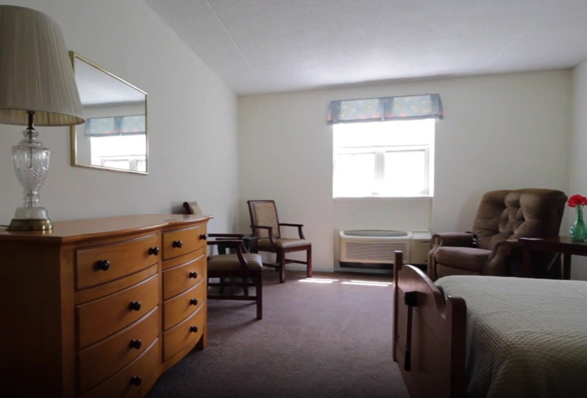 A simple bedroom with a dresser, chairs, and a window.