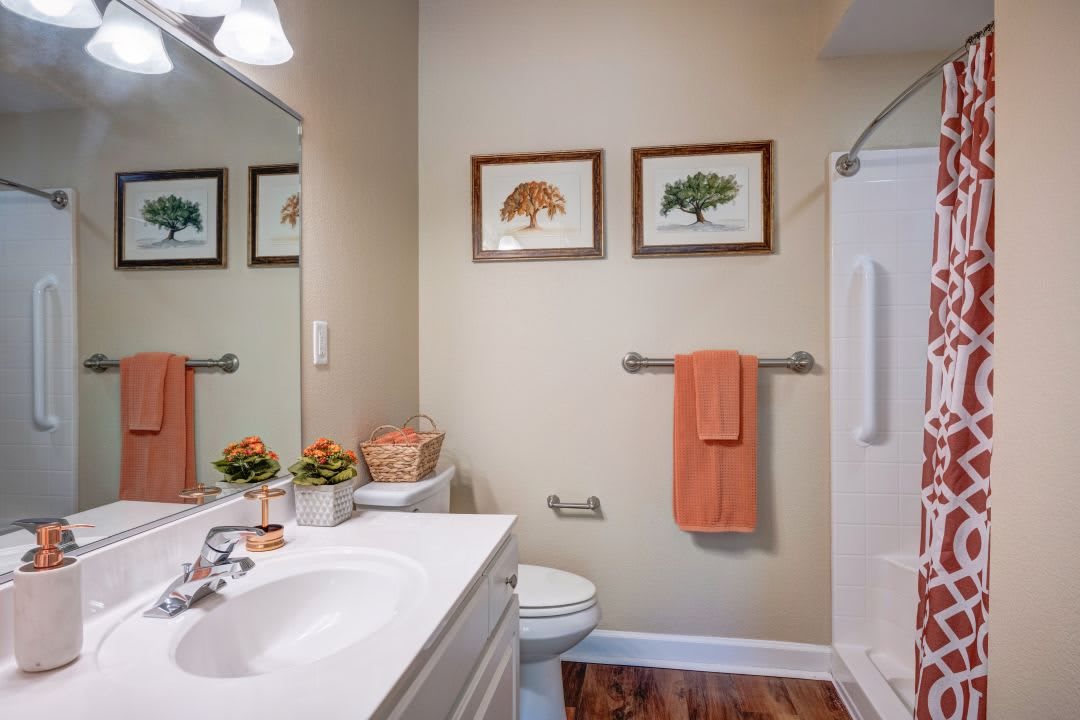 A neatly arranged bathroom featuring a sink, toilet, shower, and framed art on the wall.