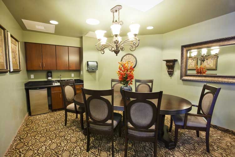 A cozy dining area with a round table, elegant chairs, and a chandelier, complemented by a kitchenette and a decorative flower arrangement.
