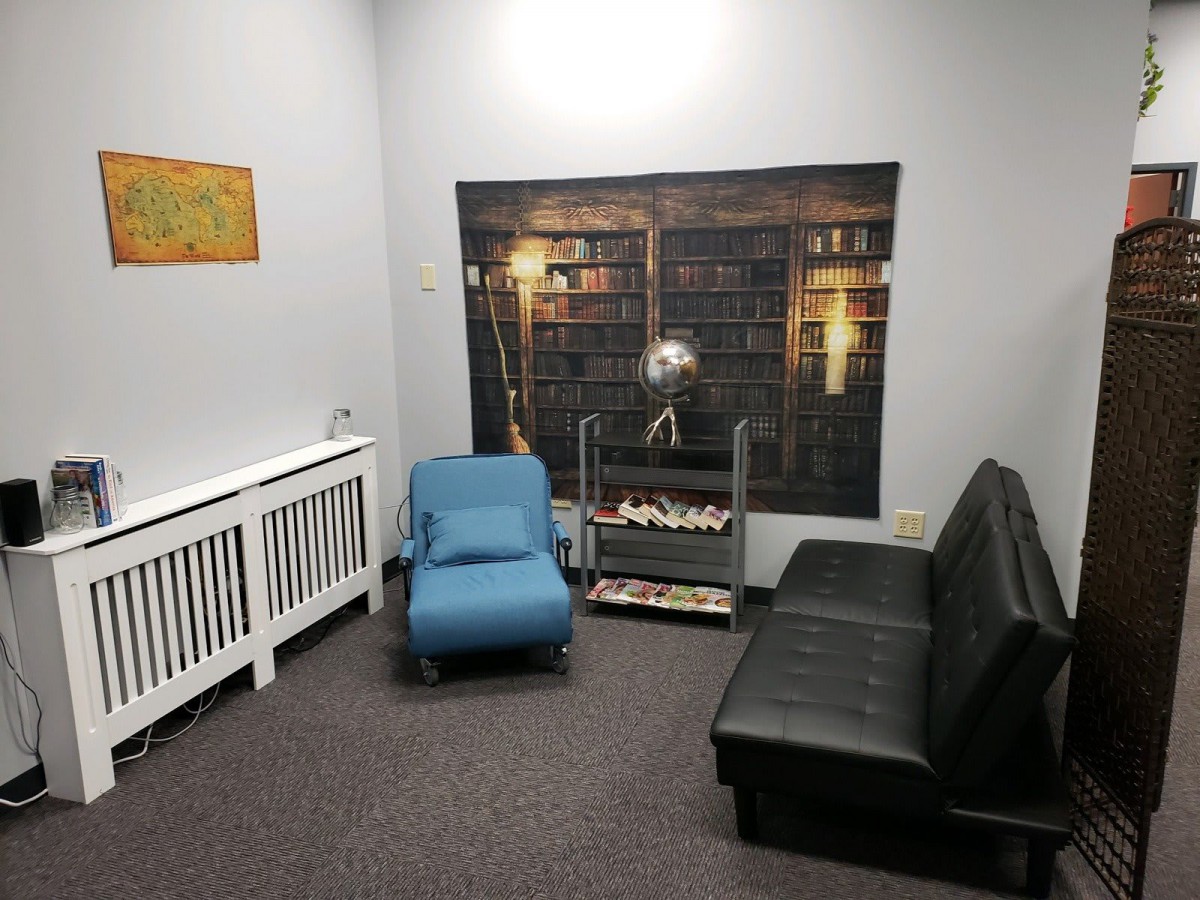 A cozy living room with a blue chair, black sofa, and bookshelf-themed decor.