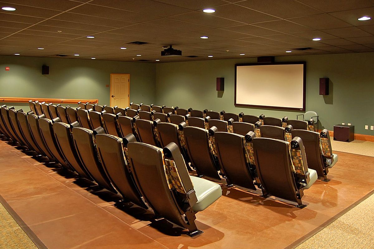 An empty theater room with rows of seats facing a large projection screen.