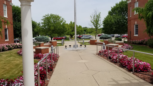 A serene park setting featuring a flagpole surrounded by vibrant flowers and lush greenery.