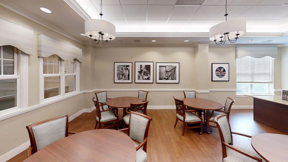 A well-lit dining area featuring round tables and cushioned chairs, adorned with framed artwork on a neutral-toned wall.