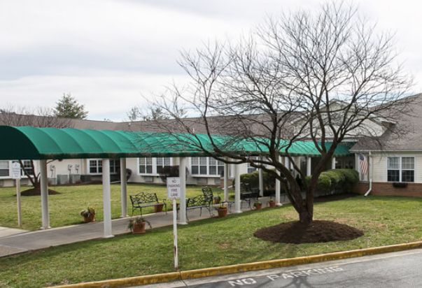 A building with a green canopy over a pathway, surrounded by a lawn and trees.