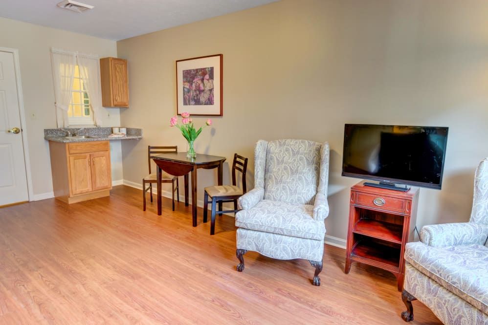 A cozy living space featuring a comfortable armchair, small dining table, and a television near a kitchenette.
