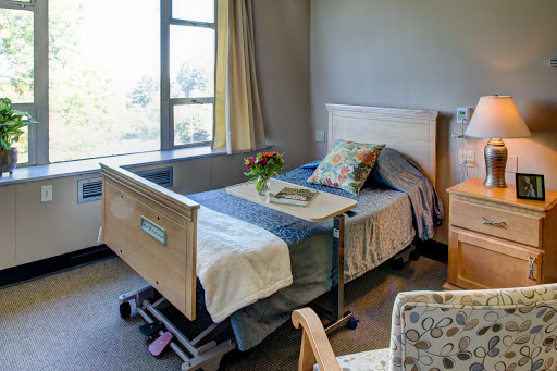 A serene hospital room featuring a neatly made bed, a window with natural light, and a small vase of flowers.