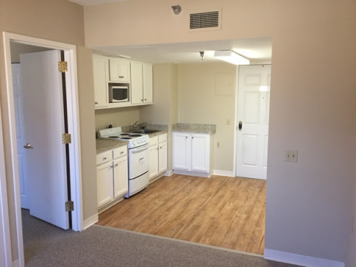 A cozy kitchen area in a modern apartment featuring white cabinetry and wooden flooring.