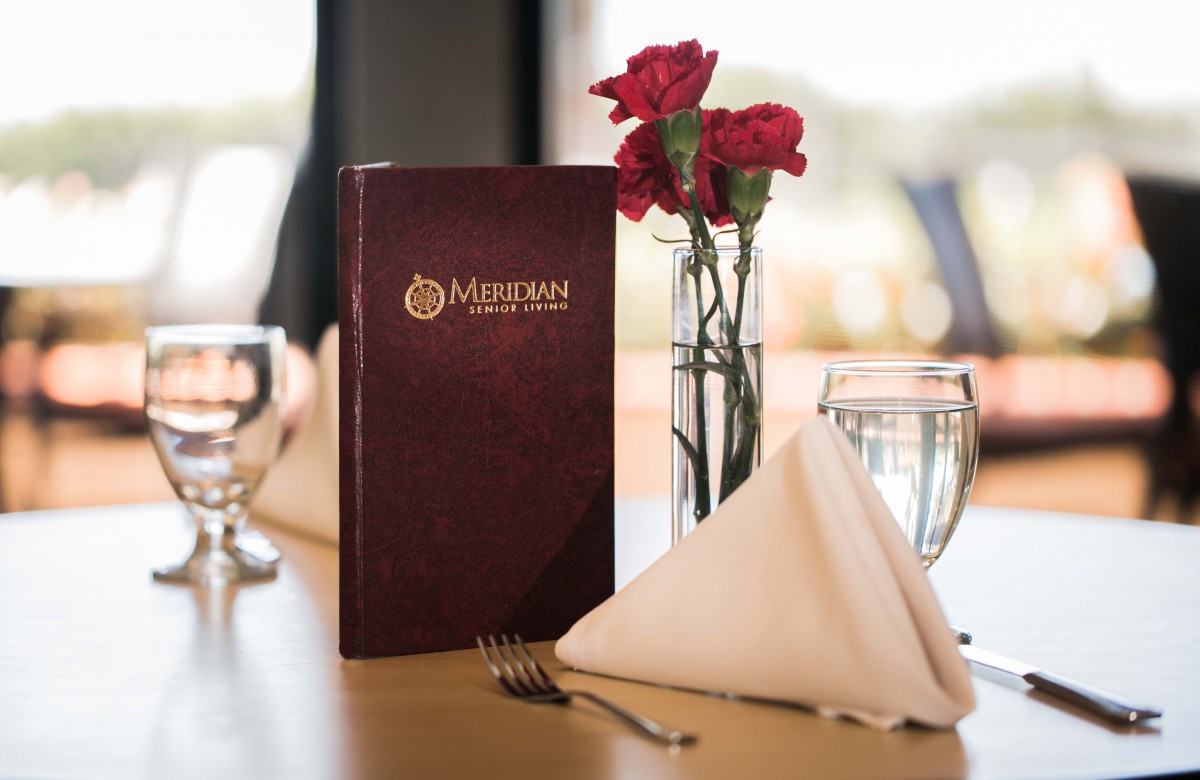 Elegant restaurant table setup with a menu, roses, and glassware.