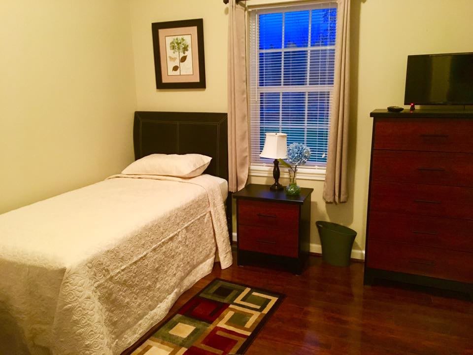 A cozy bedroom with a single bed, nightstand, and window with curtains.