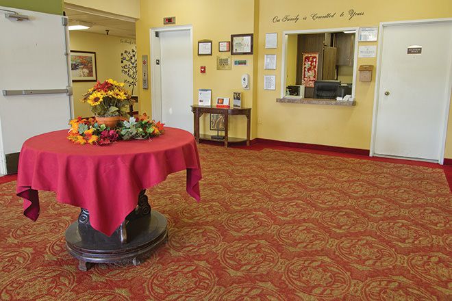 A welcoming lobby area with a red tablecloth-covered table displaying flowers, surrounded by yellow walls and carpet.