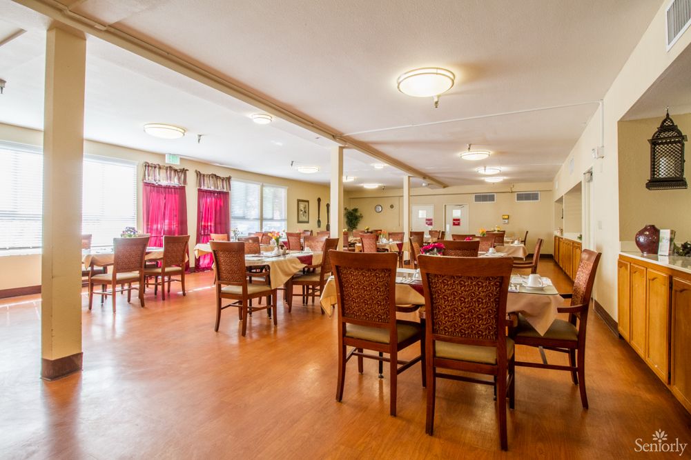 A spacious dining area with wooden tables and chairs, featuring large windows with red curtains.