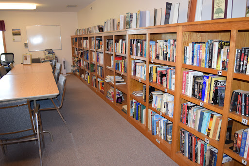 A cozy library space featuring wooden bookshelves filled with various books, accompanied by a long table and chairs for reading or studying.