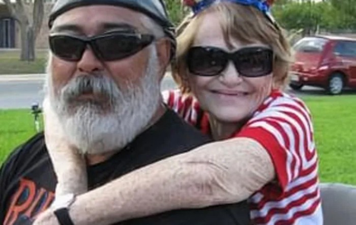 An elderly couple enjoying a sunny day together, both wearing sunglasses and smiling.