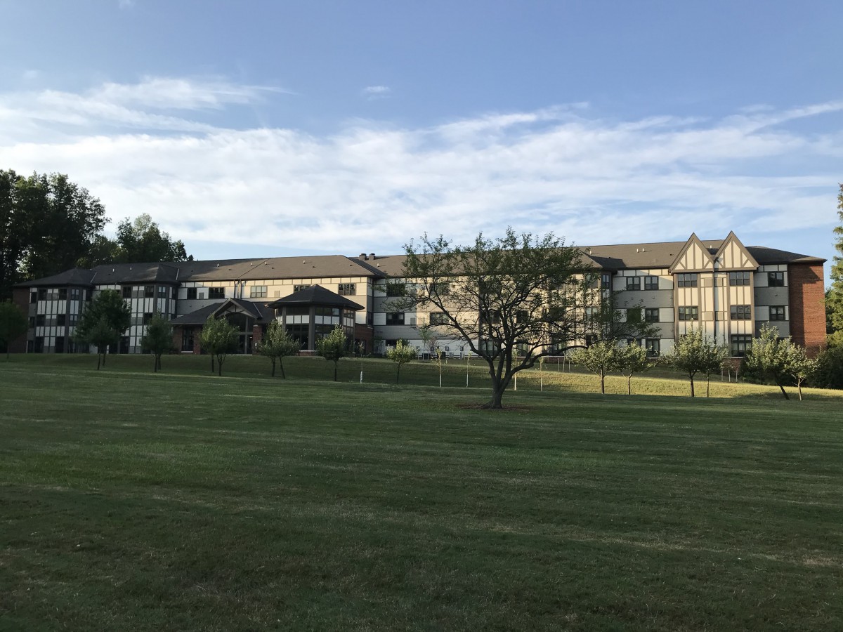 A residential building with a grassy field and trees under a cloudy sky.
