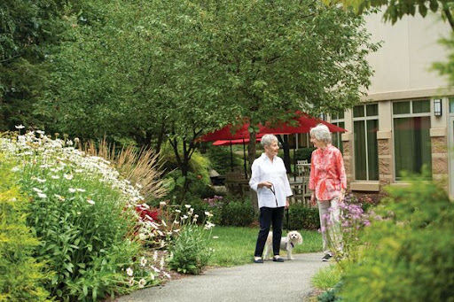 Two friends enjoy a stroll in the garden, accompanied by a small dog.