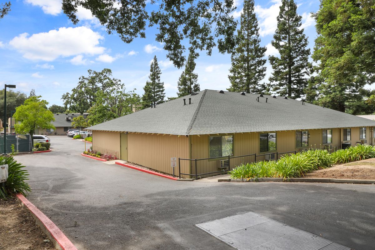 A single-story building surrounded by trees and a road under a clear blue sky.