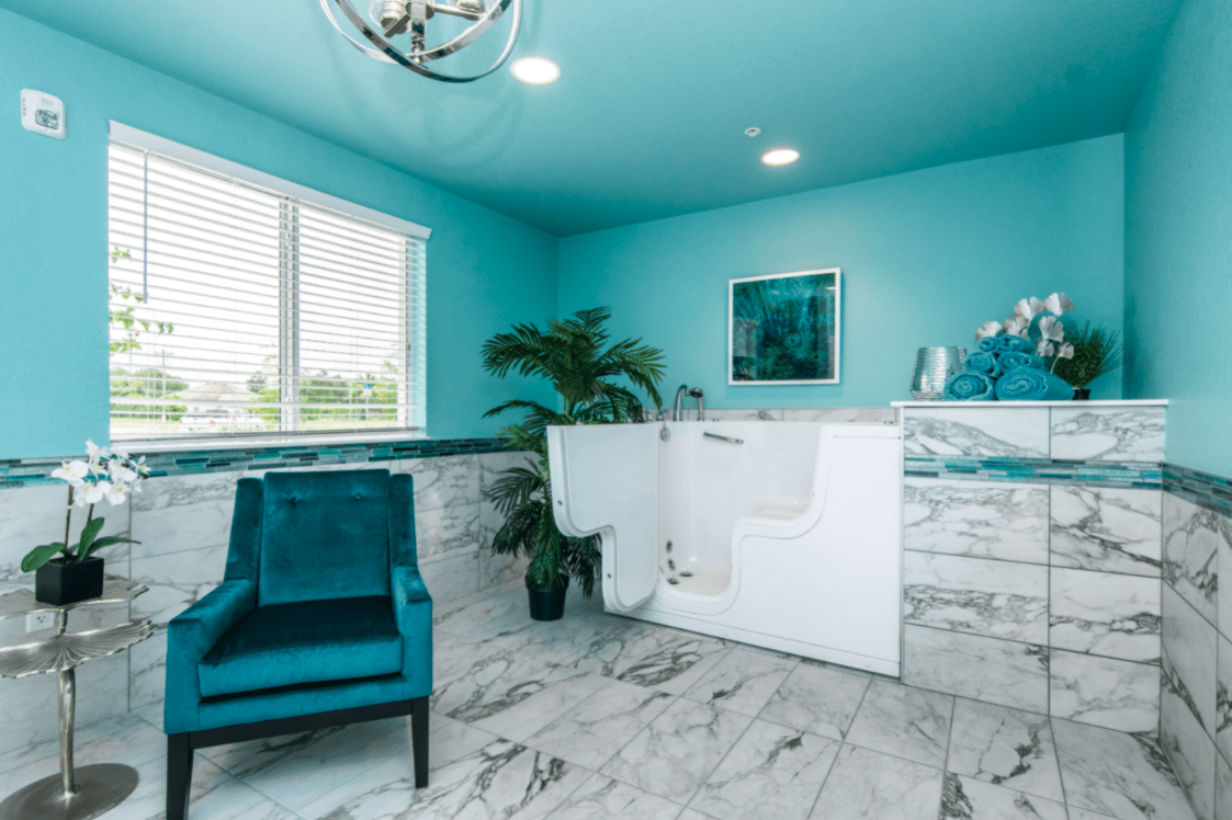 A modern bathroom with a teal color scheme, featuring a walk-in bathtub and turquoise armchair.