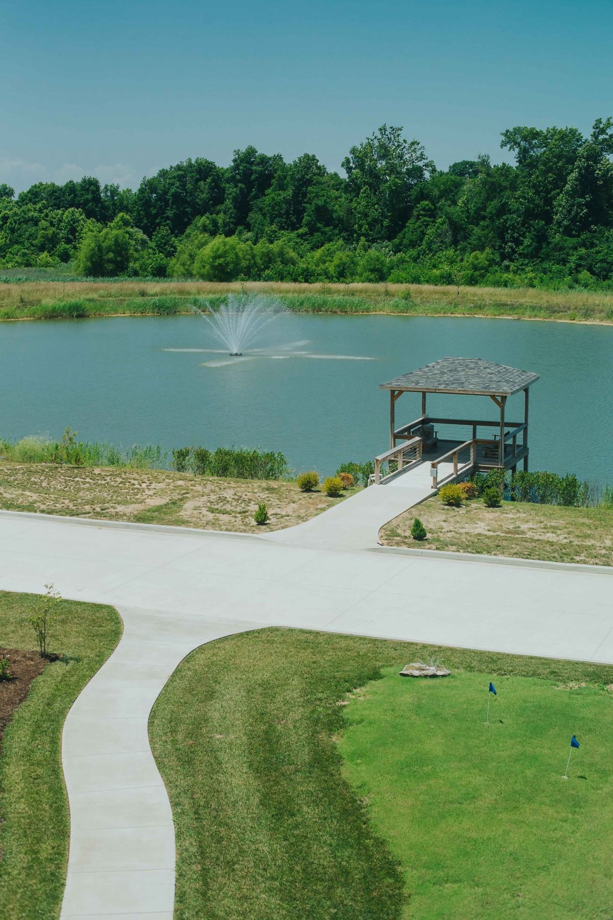 A serene landscape featuring a pond with a wooden gazebo surrounded by greenery.