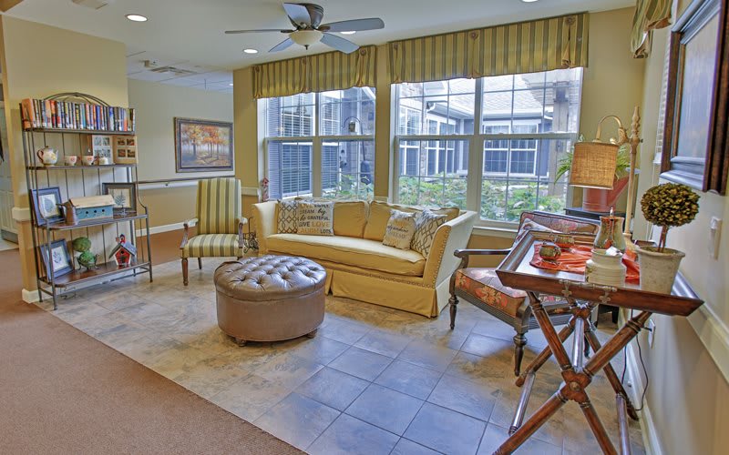A cozy living room with a sofa, armchairs, and natural light streaming through large windows.
