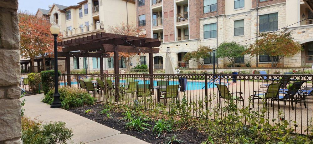 A view of an apartment complex with a fenced outdoor pool area and a pergola.