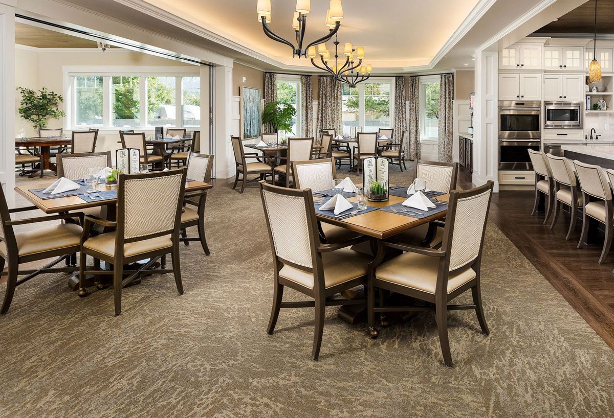 Elegant dining room with neatly arranged tables and chairs, featuring a chandelier and large windows.