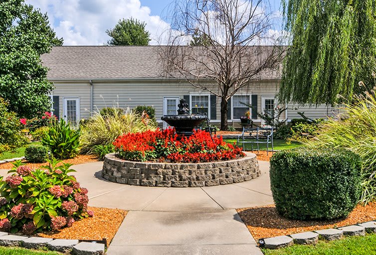 A beautifully landscaped garden with vibrant flowers and a central fountain in front of a house.