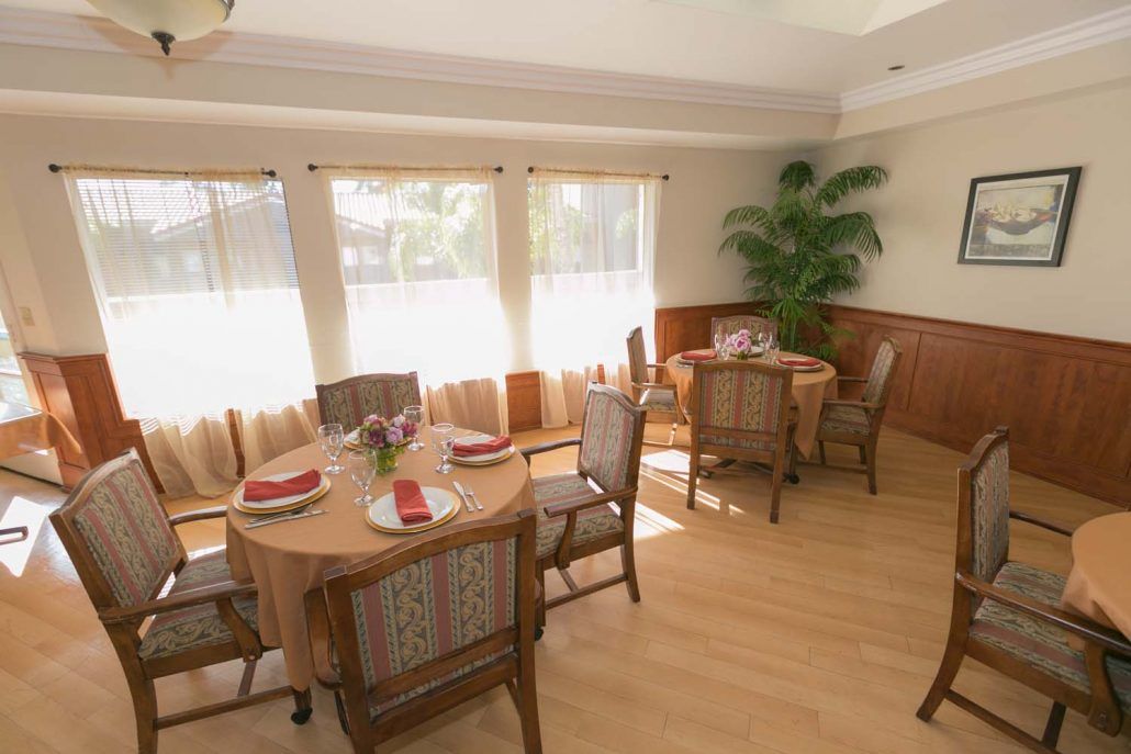 A bright dining room with neatly set tables, wooden chairs, and large windows allowing sunlight to flood the space.